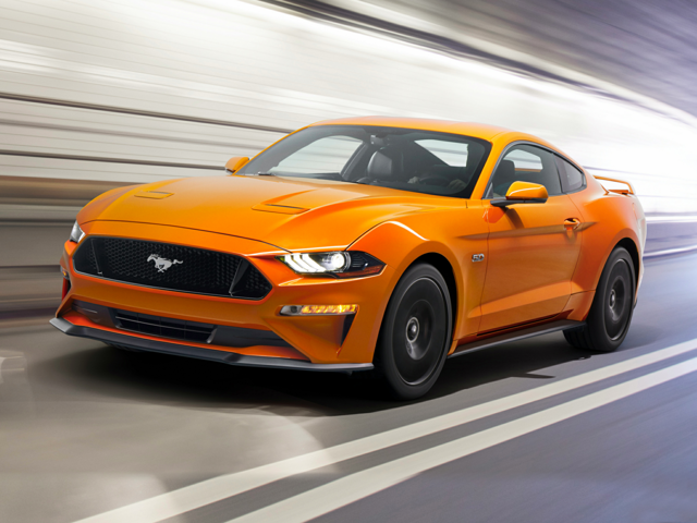An orange Ford Mustang driving on a road